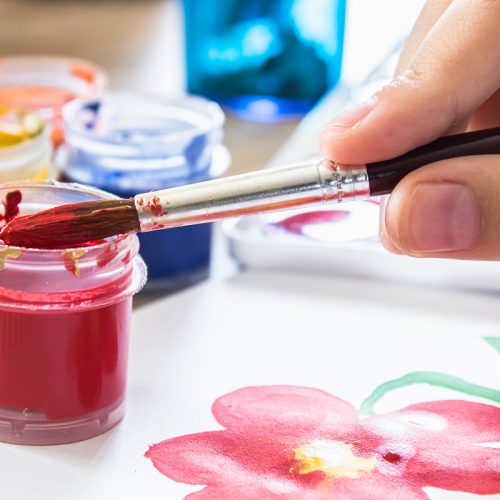The child's hands hold a brush for drawing and picks up gouache from a can. Hobbies and entertainment for children. Close-up.